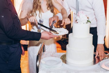 Gelin ve damat restoranda resepsiyonda lezzetli düğün pasta kesme. lüks Düğün çifti düğün kutlama Şakayık çiçekleri ile şık beyaz pasta tatmak