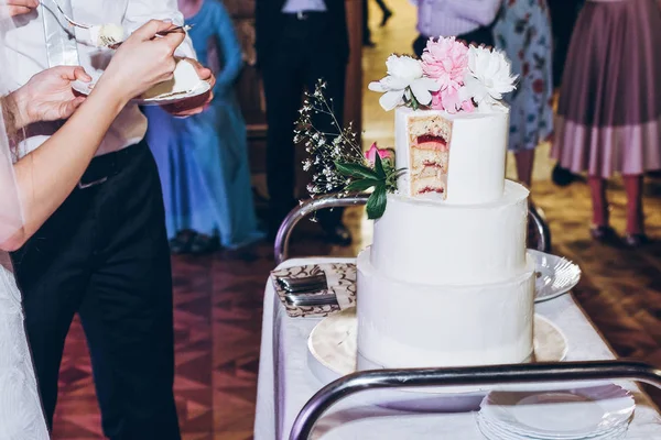 花嫁と花婿のフロント レストランでおいしいウエディング ケーキをカットします 豪華な結婚式のカップルの結婚式の祭典で牡丹の花でスタイリッシュな白いケーキの試飲 — ストック写真