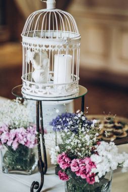 mavi ve pembe çiçekler, melek ve mum ile şık bir şekilde dekore edilmiş beyaz kuş kafesi. Düğün resepsiyonunda modern provence dekor. shabby chic