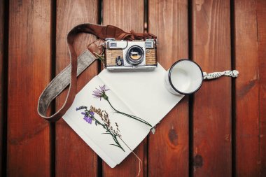 travel and wanderlust concept. photo camera, mug, notebook and wildflowers herbs on wooden background, top view. stylish traveler hipster set flat lay clipart