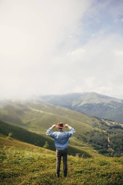 seyahat ve Yolculuk tutkusu kavramı. şık seyahat adam şapka ayakta bulutlar güneşli dağların tepesinde. metin için yer. hipster adam seyahat. muhteşem atmosferik an.