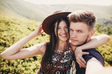 selfie alarak ve dağların üstünde tepe-in güneşli yaz gün gülümseyerek şık hipster çift. güzel erkek ve sarılma ve dağda kucaklayan şapkalı mutlu kadın. birlikte seyahat
