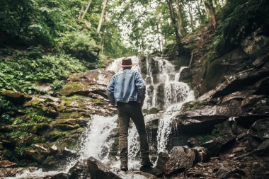 seyahat ve Yolculuk tutkusu kavramı. fotoğraf makinesi, şelale orman dağlarında ayakta ile şapkalı şık hipster adam. ormanda keşfetmek seyahat adam. metin için yer