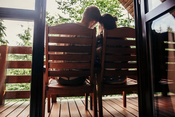 stylish hipster couple relaxing on porch, sitting in wooden cottage and looking at woods in mountains. happy family resting and embracing. summer vacation. atmospheric moment