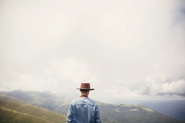 时髦的旅行者在帽子站立在阳光山的山顶在云彩 文本的空间 时髦的家伙旅行 惊人的大气时刻 旅行和流浪概念 — 图库照片
