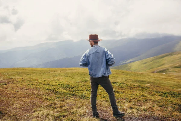 旅行和流浪概念 时髦的旅行者在帽子站立在阳光山的山顶在云彩 文本的空间 时髦的家伙在山上旅行 惊人的大气时刻 — 图库照片