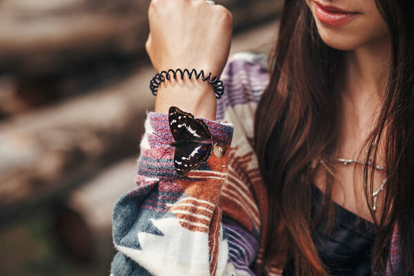 beautiful butterfly on girl hand. stylish hipster,happy woman in hat holding apatura iris  on fingers in forest in mountains. travel and wanderlust concept. space for text. amazing moment