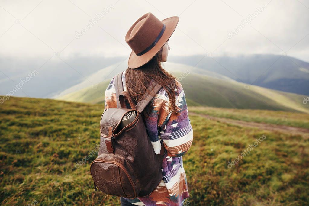 traveler hipster girl in hat with backpack exploring misty sunny mountains in clouds. space for text. stylish woman traveling. amazing atmospheric moment. travel and wanderlust concept.