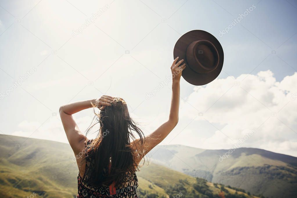 travel and wanderlust concept. traveler hipster girl holding hat, looking at sunny mountains. summer vacation. space for text. amazing atmospheric moment. happy woman traveling