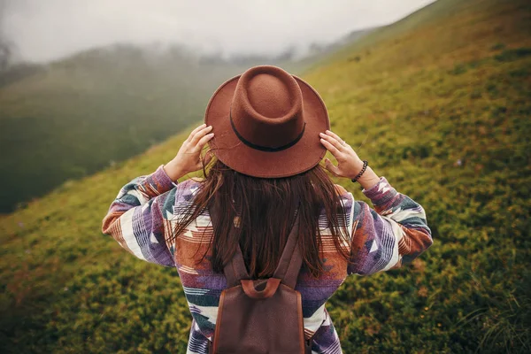 快乐的旅行者时髦的女孩拿着帽子 漫步在阳光明媚的群山中 云雾缭绕 旅行和流浪概念 文本的空间 大气时刻 妇女旅行 — 图库照片