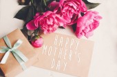 šťastné matky den text na kartě řemesla a kytice růžové pivoňky s krabičky na rustikální bílé dřevěné pozadí ve světle. Květinový pozdrav card koncept, plochý ležela. den matek