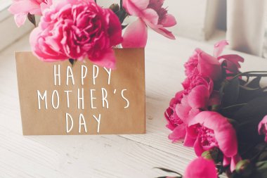 mutlu anneler günü metin craft kartı ve pembe peonies buket ışık beyaz rustik ahşap pencere üzerinde. çiçek tebrik kartı kavramı. Anneler günü. Yumuşak ihale bahar görüntü
