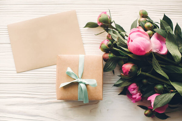 lovely pink peonies with empty craft card and gift box on rustic white wooden background top view
