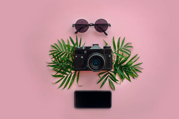stylish black photo camera with green palm leaves, sunglasses and phone on trendy pink background, flat lay. modern hipster travel image. summer vacation,space for text