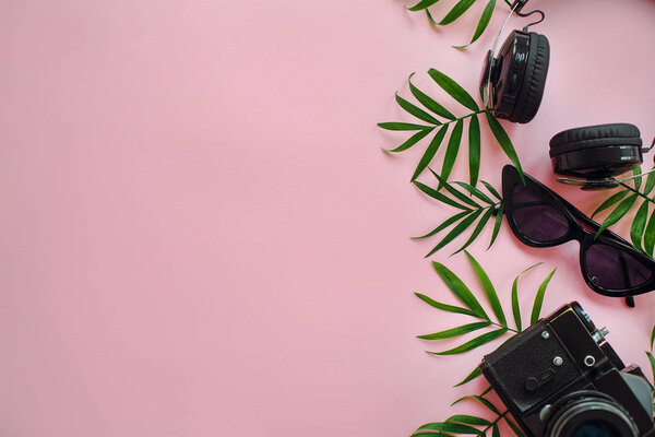 summer vacation flat lay, space for text. stylish black photo camera with green palm leaves, sunglasses and headphones on trendy pink background. modern hipster travel  image.
