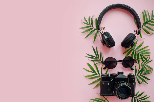 summer vacation flat lay, space for text. stylish black photo camera with green palm leaves, sunglasses and headphones on trendy pink background. modern hipster travel  image.