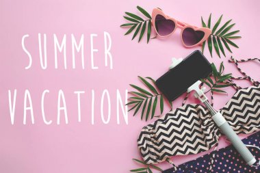 Yaz tatili metin şık pembe güneş gözlüğü, modern mayo, telefon selfie Stick pembe arka plan yeşil palmiye yaprakları. zaman kavramı seyahat için. şık yaz düz yatıyordu.