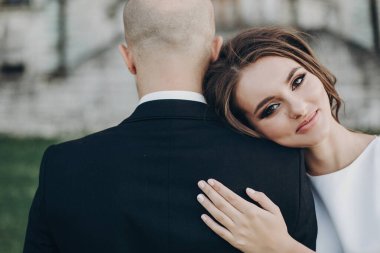 Parktaki eski şatonun yakınında akşam güneşinde kucaklaşan muhteşem gelin ve damat. Romantik bir an. Şık bir düğün çifti nazikçe sarılıyor ve gülümsüyor.
