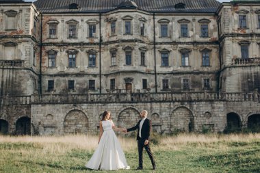 Güzel parktaki eski şatonun yakınlarında güneş ışığında yürüyen muhteşem bir düğün çifti. Tarz sahibi güzel gelin ve damat el ele tutuşuyorlar.