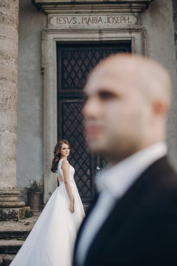 Parktaki eski şatonun yanındaki taş merdivenlerde poz veren muhteşem bir çift. Tarz sahibi, harika bir gelinlik içinde, eski bina ve doğa arka planında damada bakan güzel bir gelin.