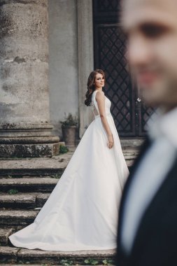 Parktaki eski şatonun yanındaki taş merdivenlerde poz veren muhteşem bir çift. Tarz sahibi, harika bir gelinlik içinde, eski bina ve doğa arka planında damada bakan güzel bir gelin.