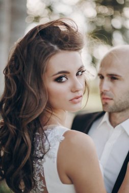 Parktaki eski şatonun yakınında akşam güneşinde kucaklaşan muhteşem gelin ve damat. Romantik bir an. Şık bir düğün çifti nazikçe sarılıyor ve gülümsüyor.