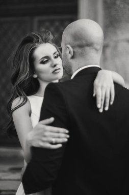 Parktaki eski şatonun yakınında akşam güneşinde kucaklaşan muhteşem gelin ve damat. Romantik bir an. Şık bir düğün çifti nazikçe sarılıyor ve gülümsüyor.