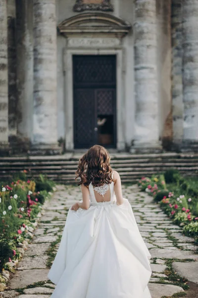 漂亮的新娘穿着漂亮的长袍走向公园里的古堡 穿着华丽的白色婚纱的时髦新娘的后面 浪漫的时刻 — 图库照片