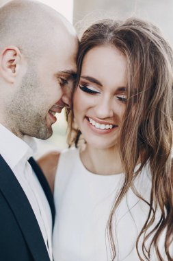 Parktaki eski şatonun yakınında akşam güneşinde kucaklaşan muhteşem gelin ve damat. Romantik bir an. Şık bir düğün çifti nazikçe sarılıyor ve gülümsüyor.