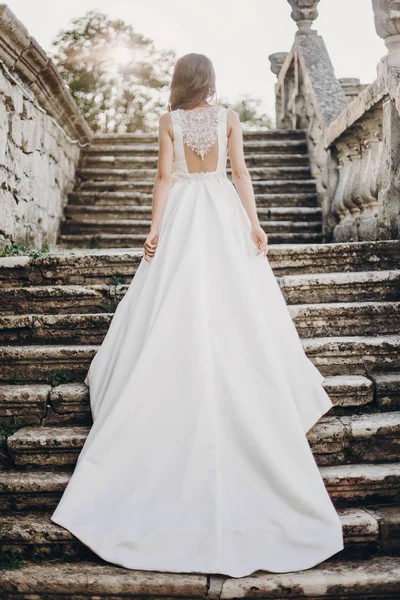 穿着华丽的白色婚纱的新娘站在楼梯上 漂亮的新娘穿着华丽的婚纱走向公园里的古堡 浪漫的时刻 — 图库照片