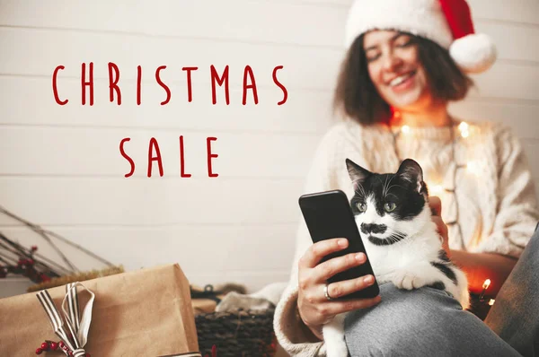 Χριστούγεννα Sale κείμενο σημάδι στη γάτα κοιτάζοντας την οθόνη του τηλεφώνου με διασκέδαση — Φωτογραφία Αρχείου