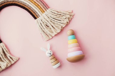 Bebek için çevre dostu plastik oyuncaklar. Pembe arka plandaki çocuklar için ahşap oyuncaklar. Modern renkli ahşap piramit halkalar, ahşap tavşan ve makrome gökkuşağı.