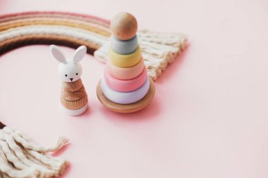 Bebek için çevre dostu plastik oyuncaklar. Pembe arka plandaki çocuklar için ahşap oyuncaklar. Modern renkli ahşap piramit halkalar, ahşap tavşan ve makrome gökkuşağı.