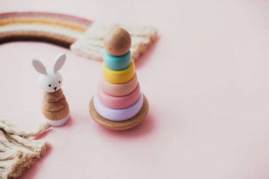 Pembe arka plandaki çocuklar için ahşap oyuncaklar. Yüzüklü, ahşap piramit, ahşap tavşan ve makrome gökkuşağı. Bebek için çevre dostu plastik oyuncaklar