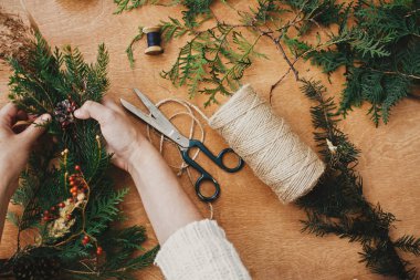 Noel çelengi atölyesi. Köknar dalları, çam kozalakları tutan eller