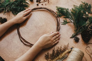 Noel çelengi yapıyorum. Eller ahşap daire ve köknar sütyen tutuyor.