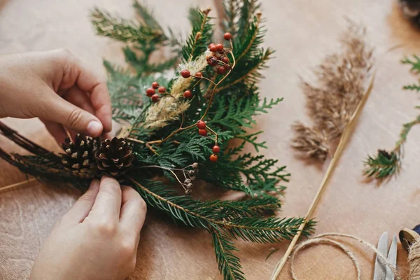 Fazendo grinalda de Natal rústica. Mãos segurando pinhas, berrie — Fotografia de Stock