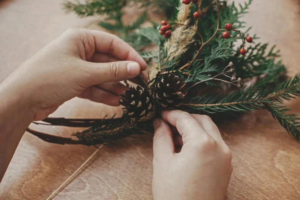 Machen rustikalen Weihnachtskranz. Hände, die Tannenzapfen halten, berrie — Stockfoto
