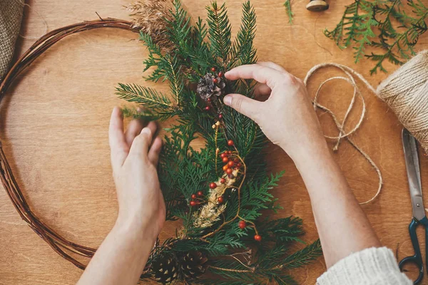 Kırsal Noel çelengi düzleştiriyor. Eller köknar dalını tutuyor