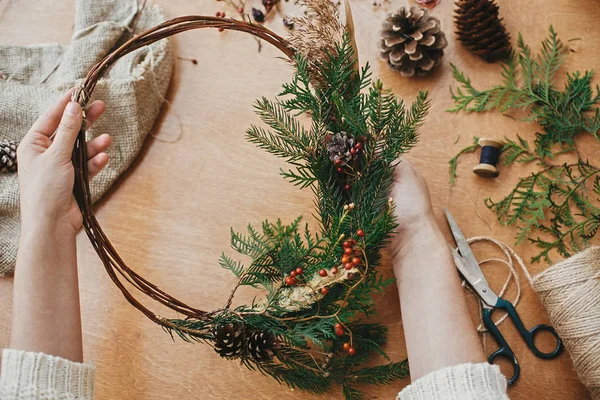Mãos segurando grinalda de Natal rústica com cones de pinho, bagas , — Fotografia de Stock