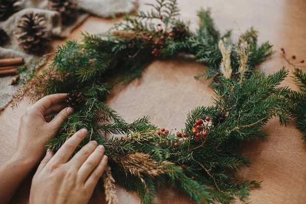 Ruce držící vánoční věnec s jedlovými větvemi, bobulemi, borovicemi — Stock fotografie