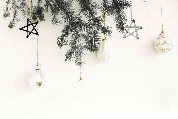 Κομψά χριστουγεννιάτικα στολίδια σε κλαδί ελάτης που κρέμονται σε λευκό τοίχο. — Φωτογραφία Αρχείου