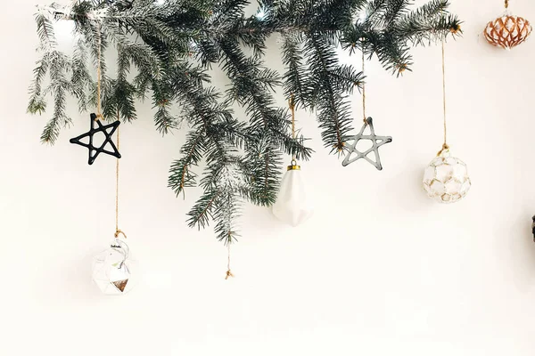 Stilvoller Weihnachtsschmuck hängt an Tannenzweig an weißer Wand. — Stockfoto