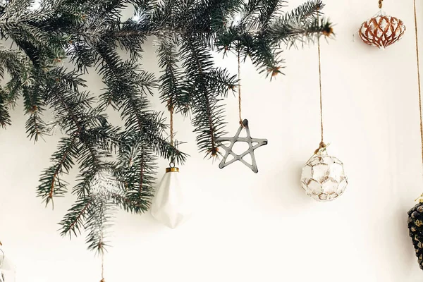 Elegantes adornos de Navidad colgando de la rama de abeto en la pared blanca . —  Fotos de Stock