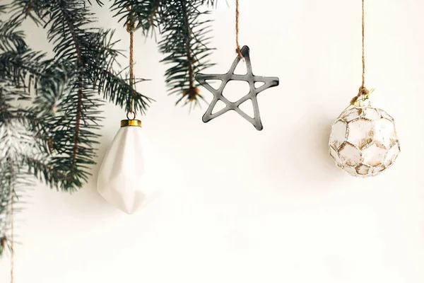 Eleganti ornamenti natalizi appesi al ramo di abete sulla parete bianca . — Foto Stock