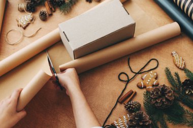 Makas ve hediye kutusuyla ambalaj kağıdı kesen eller.