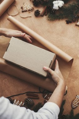 El işi kağıt ve çam dallarıyla Noel hediyesini paketleyen eller, 