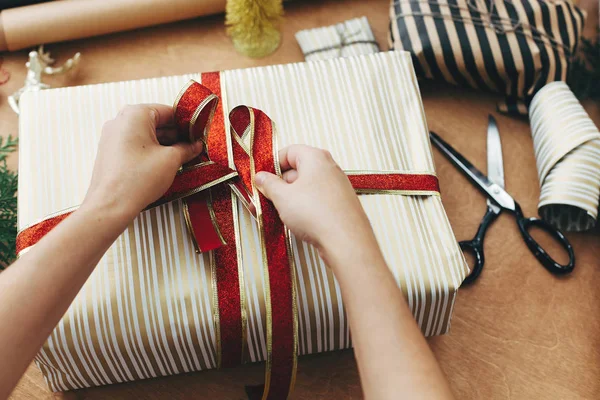 Eller kırmızı kurdele tutuyor ve şık hediye kutusunu şeritle kaplıyor.