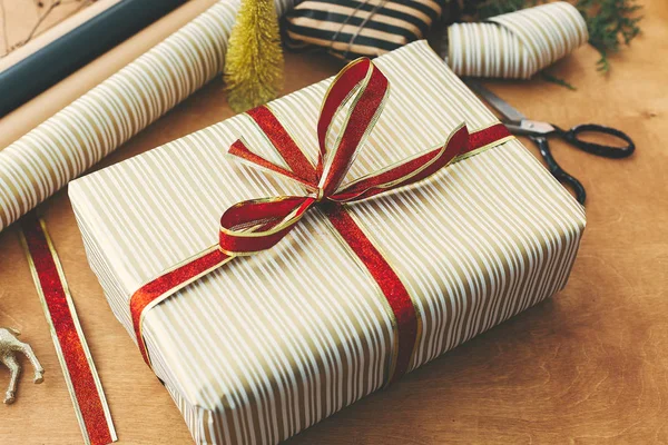 Kırmızı kurdeleli çizgili altın kağıt içinde şık bir Noel hediyesi kutusu. — Stok fotoğraf