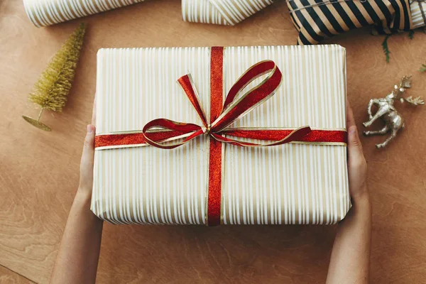 Mãos dando caixa de presente de Natal elegante em papel dourado listrado — Fotografia de Stock